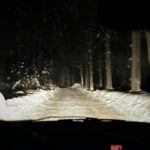 Nocna jazda przez ośnieżony las, droga oświetlona światłami auta
