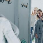 Dwie kobiety w przymierzalni, jedna mierzy płaszcz, druga doradza