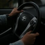 Kierowca trzyma kierownicę Toyoty, wnętrze auta w przyciemnionym świetle