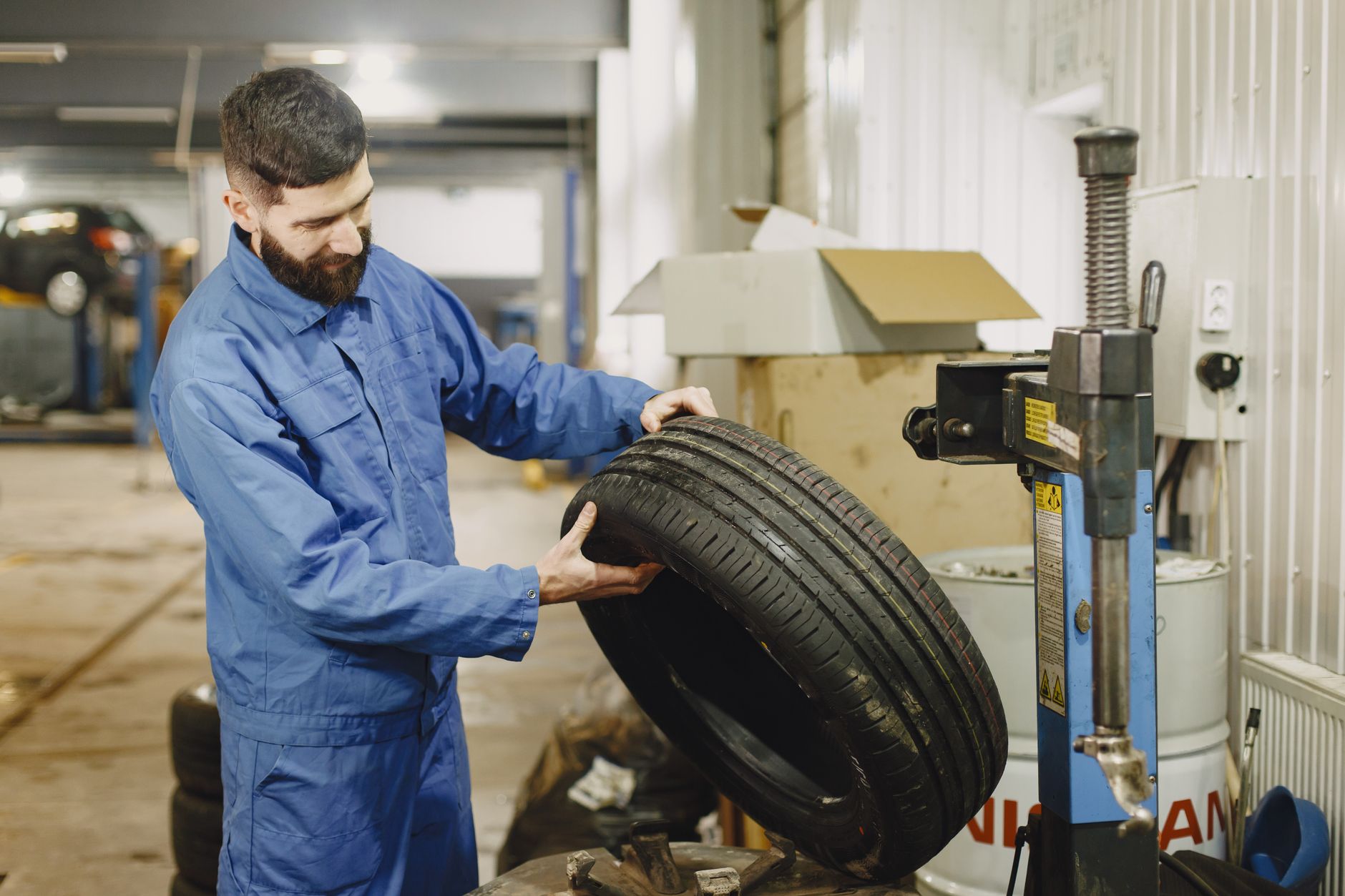 Mechanik w niebieskim kombinezonie sprawdza oponę w warsztacie samochodowym
