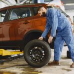 Mechanik w niebieskim kombinezonie wymienia oponę w czerwonym SUV-ie