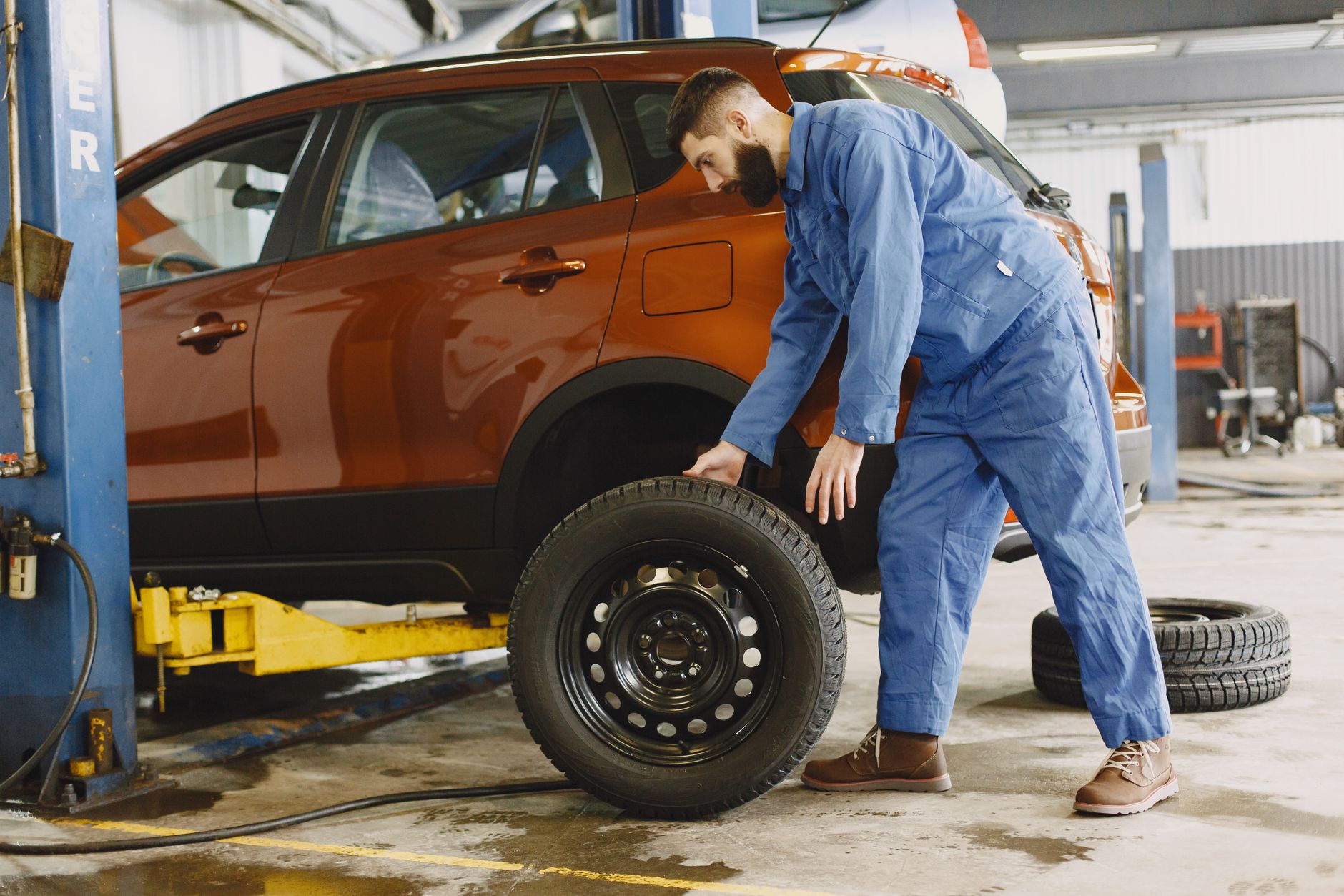 Mechanik w niebieskim kombinezonie wymienia oponę w czerwonym SUV-ie